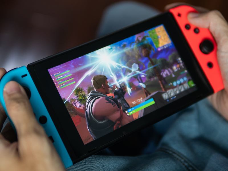 A close-up of a person’s hands holding a Nintendo Switch with the Fortnite game playing on it.