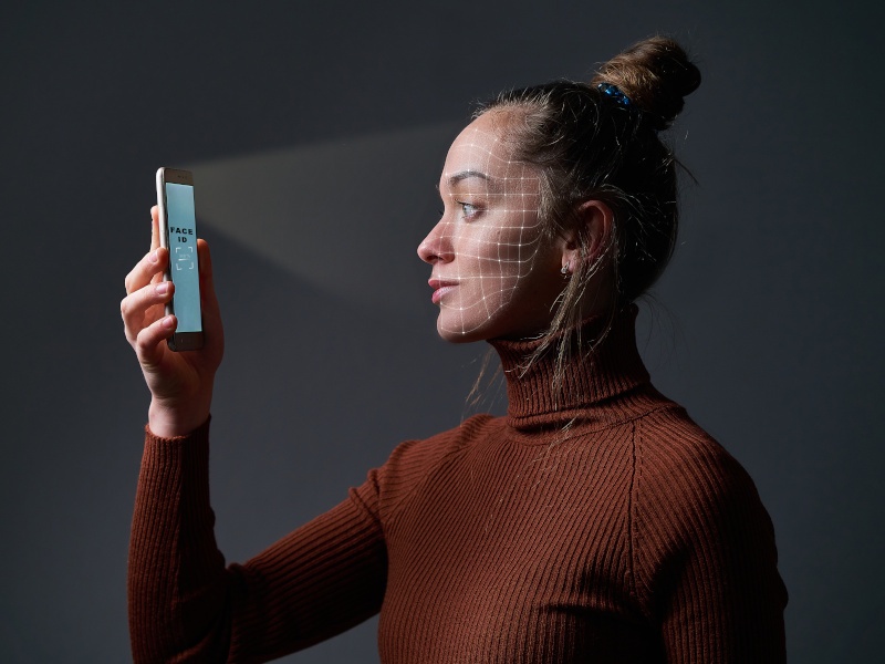 Woman scans face using facial recognition system on mobile phone for biometric identification.