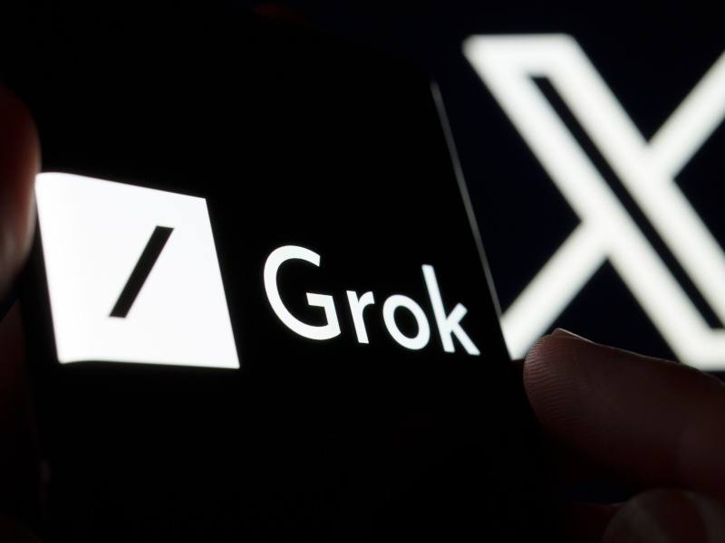 The X logo in the background and the Grok logo on a smartphone in the foreground.