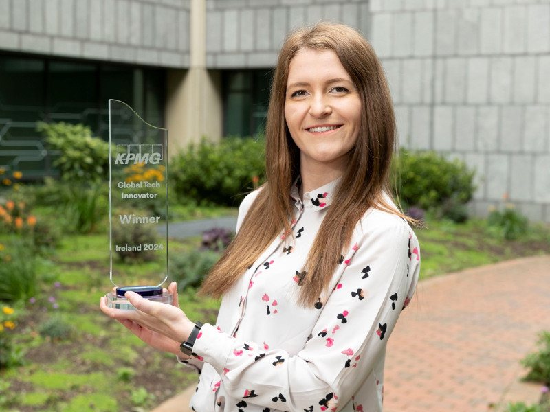 A woman wearing a patterned white blouse smiles while holding the KPMG Global Tech Innovator Ireland award.