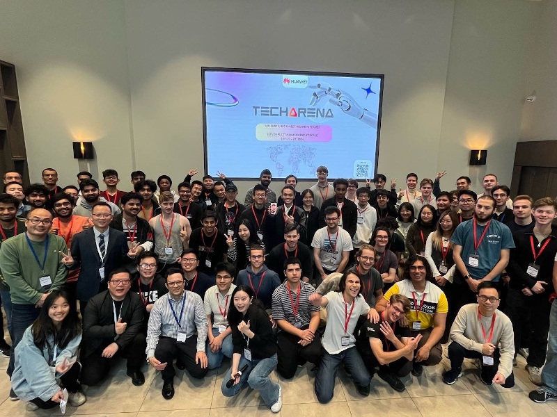 A large group of students gathered together wearing lanyards and standing in front of a large screen that says Huawei Tech Arena.