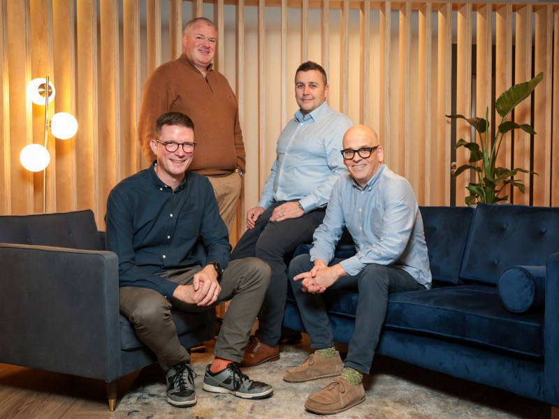 Four men from Instil and Vertical Structure gathering in a bright room, with two sitting and two standing.