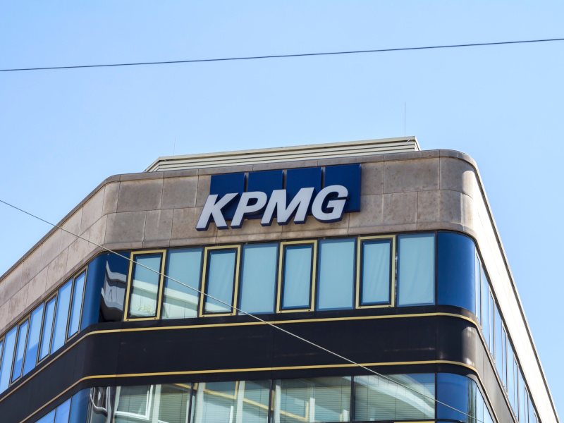 A shot looking up at the KPMG sign on the top of an office building against a blue sky.