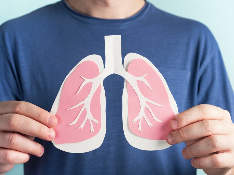 A man wearing a blue t-shirt holds a paper cutout of lungs in front of his chest, to symbolise lung cancer research.