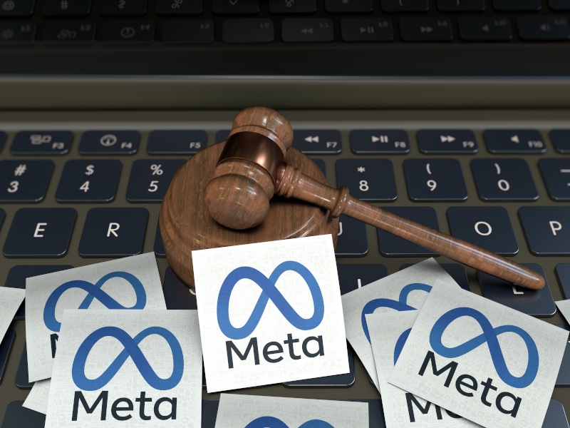 A mini judge’s gavel sits on a laptop keyboard with small square pieces of paper with the Meta logo on them scattered across it.