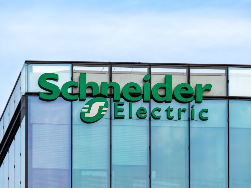 A green Schneider Electric logo at the top of a large glass building against a blue sky.