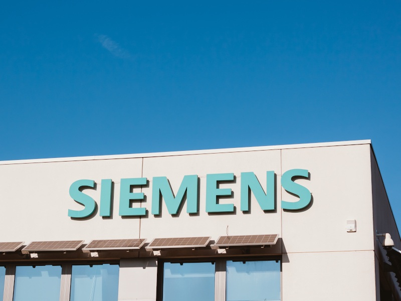 The Siemens company logo on a grey office building against a clear blue sky.