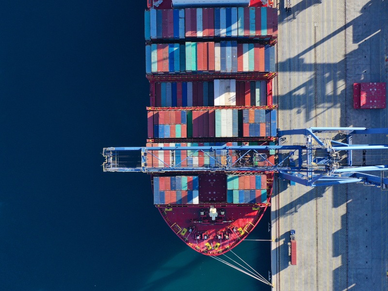 An aerial shot of a ship being loading with containers at a dock.