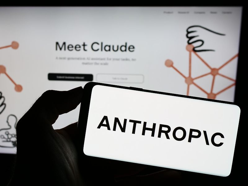 The Anthropic logo on a phone screen with the Claude interface on a screen in the background.