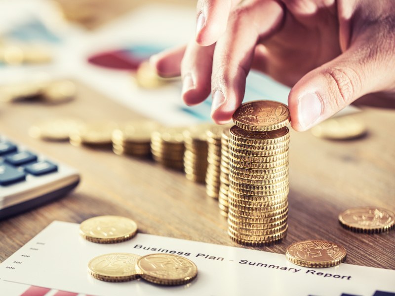 A woman's hand is stacking fifty cent coins on a table next to a calculator and a sheet of paper with 'business plan' written on it.