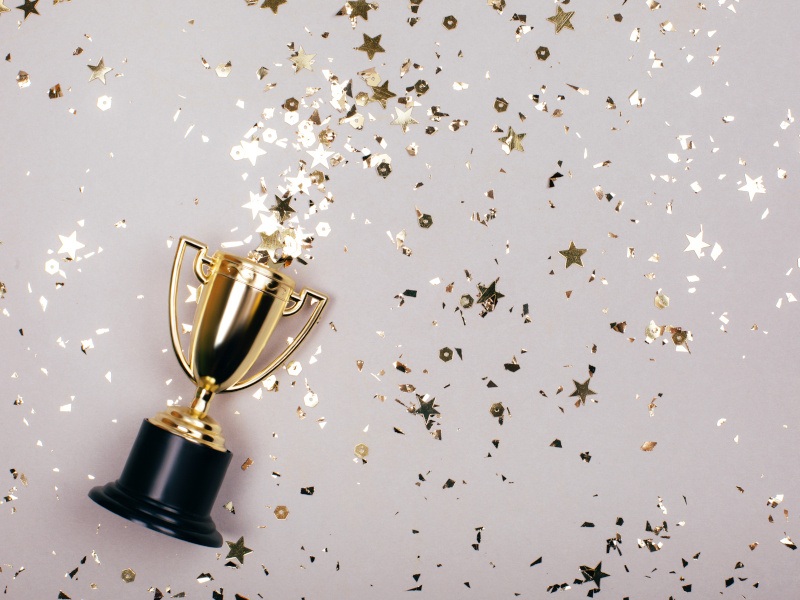 Beige background with gold confetti around and a gold winner's cup.