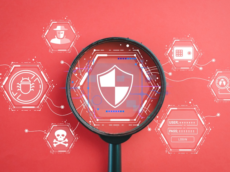 A red background and a black magnifying glass in the centre with cyber related vector images all around.