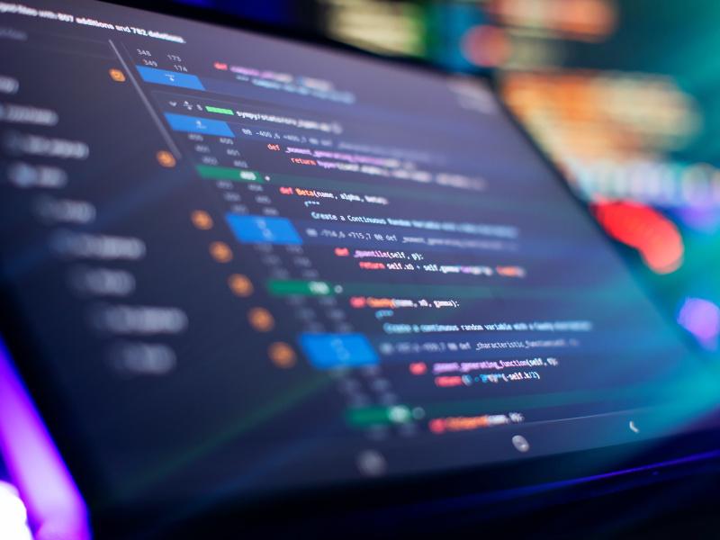 A close-up of a tilted computer screen with lines of colourful code on it to represent software development.