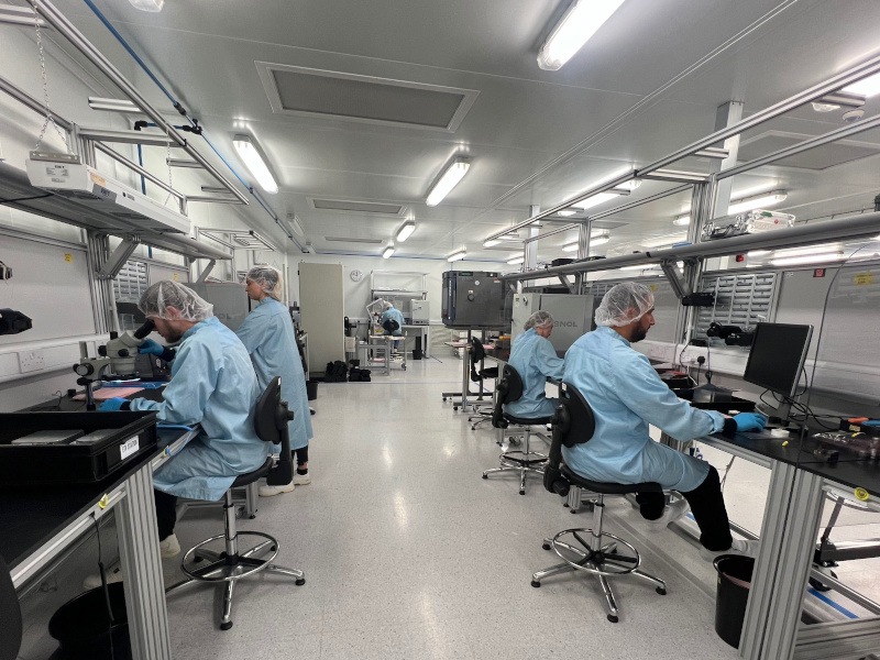 Four people sit along two workstations wearing protective gear working on technology.