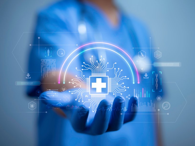 The blurry torso of a person in scrubs holding out a gloved hand towards the camera with digital health symbols overlaid on the image to show health data and AI concepts.