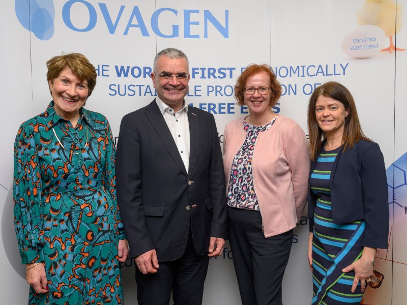 Four people standing in front of a poster, smiling.