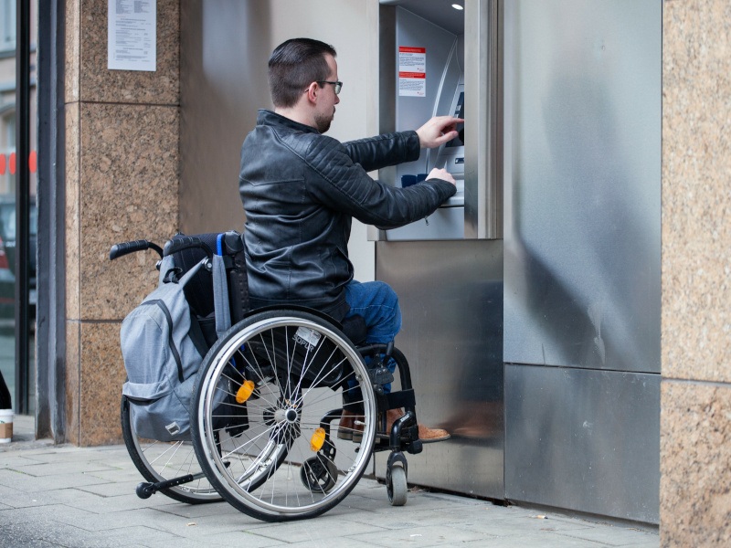 A man in a wheelchair using an ATM bank machine.