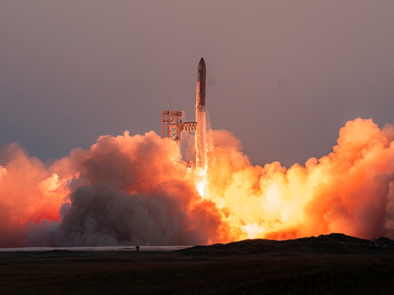 The SpaceX starship launching in a blaze of fire and smoke.