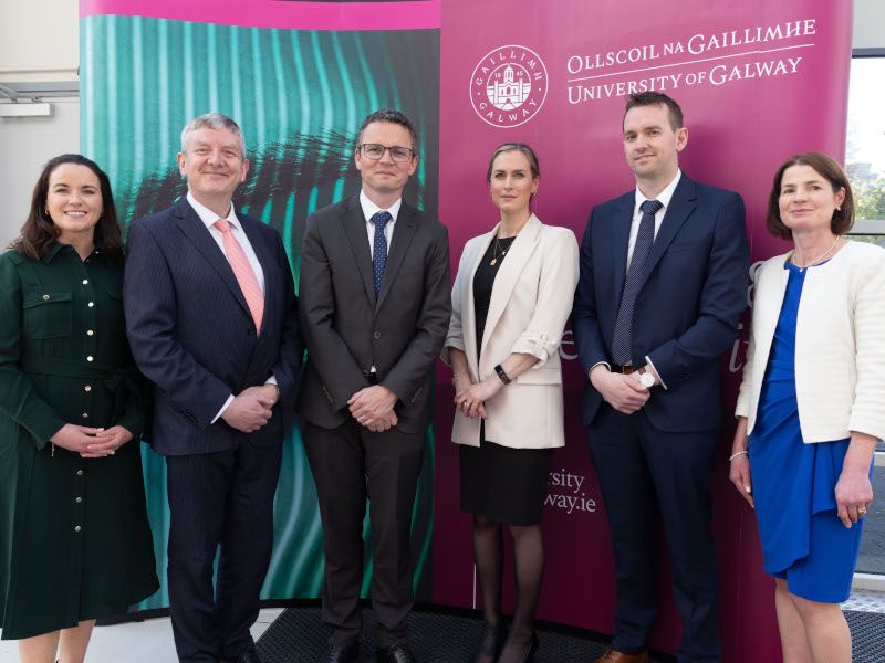 Six people standing in front of the University of Galway poster.