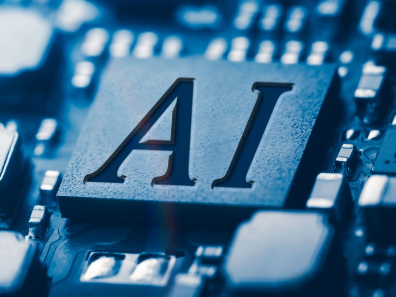 A circuit board with a square in the middle of it. The letters ‘AI’ are on the square, standing for artificial intelligence.