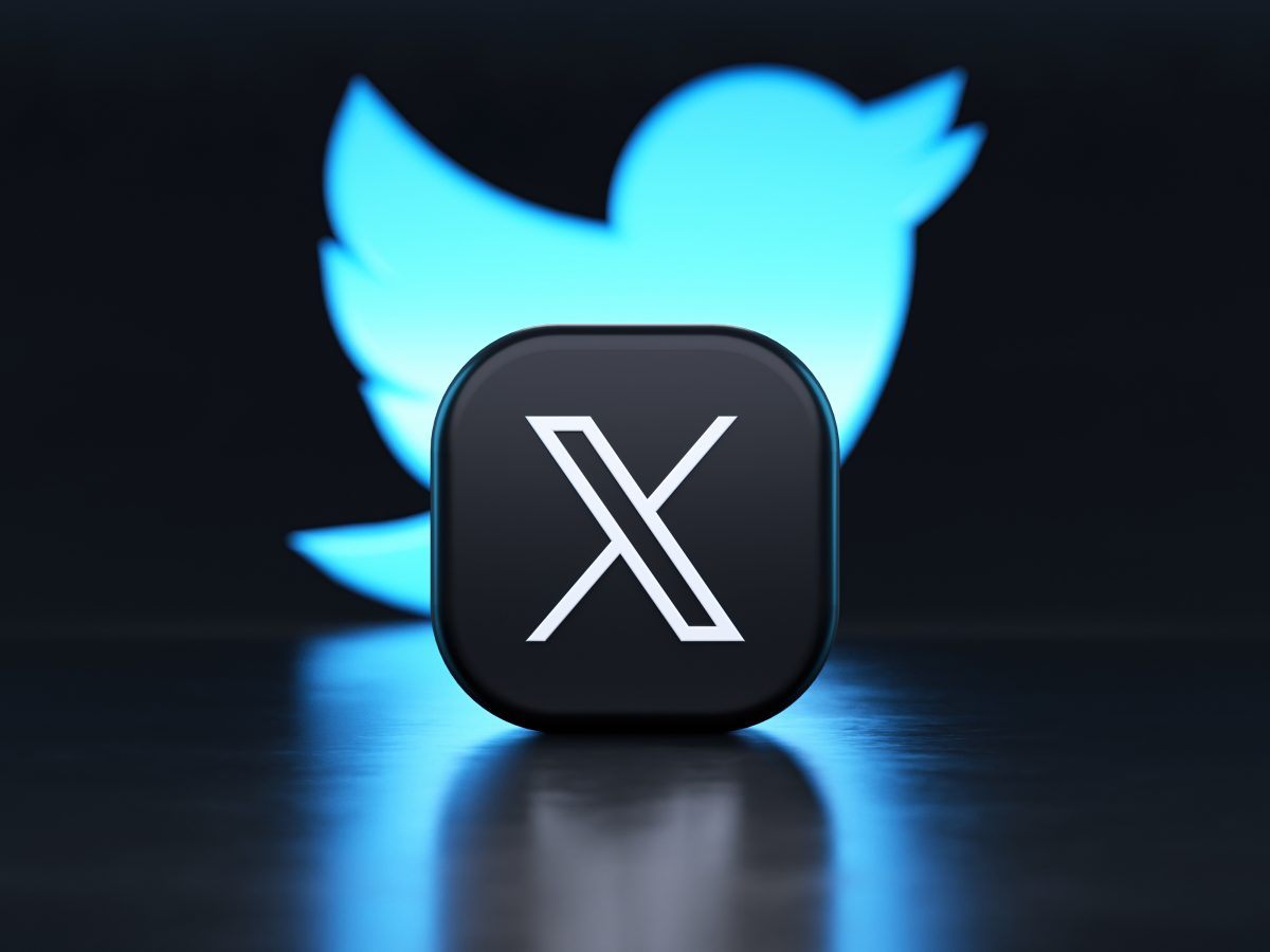 A black X logo is placed in front of a neon blue sign showing the former blue bird logo of the social media website Twitter.