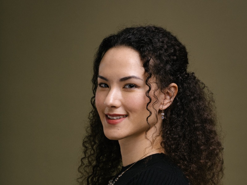 A headshot of a woman with curly brown hair smiling at the camera.