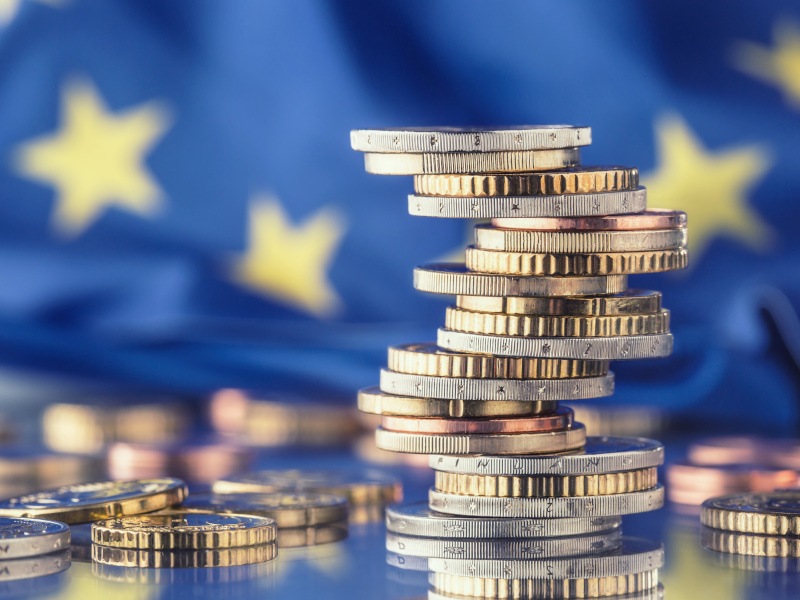 A number of silver and gold Euro coins are stacked on top of each other. There are also coins on the ground around the stack.