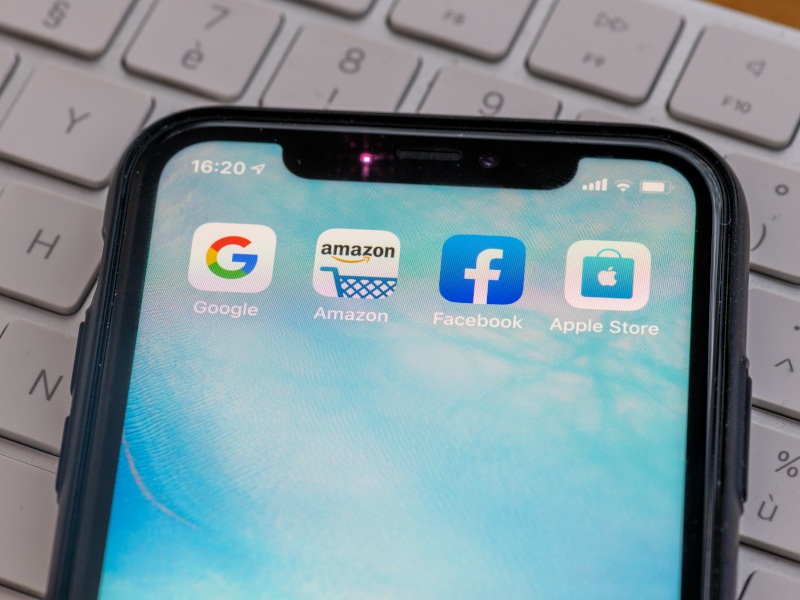 The top of a mobile phone screen. Four app shortcuts visible on it, including for Apple and Google. The phone is lying against a white keyboard.