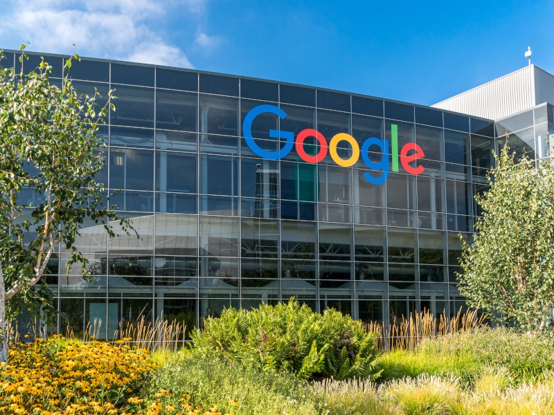 A large building with multiple windows. The ‘Google’ logo is displayed on it. Trees and plants can be seen in the image too.