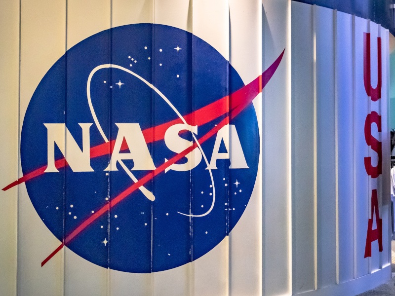 A large blue and red logo bearing the word ‘NASA’ is seen on a white wall. Beside it is another white wall with the letters ‘USA’ on it.