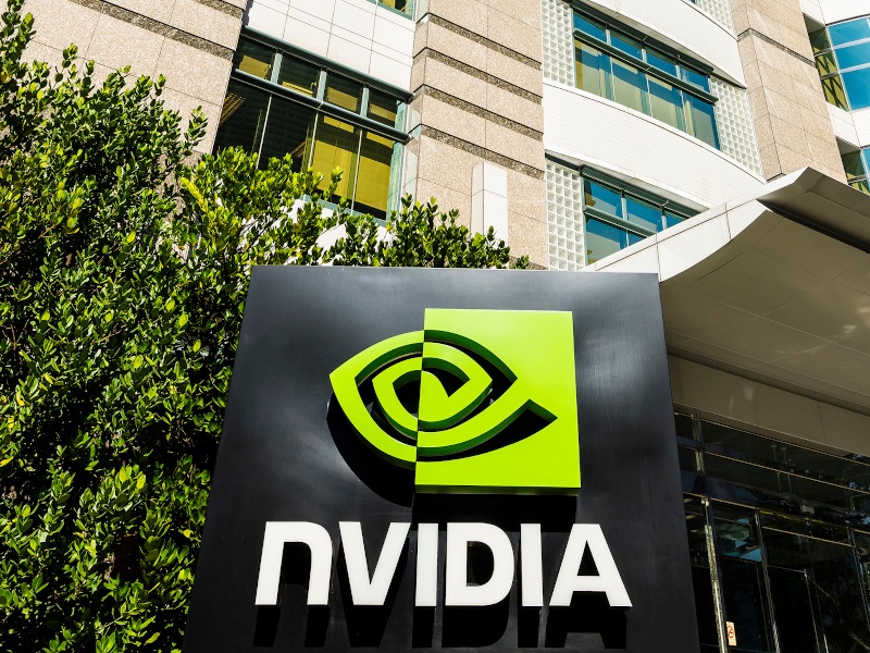 A large office building with a black sign at the front showing the Nvidia logo next to a bush.