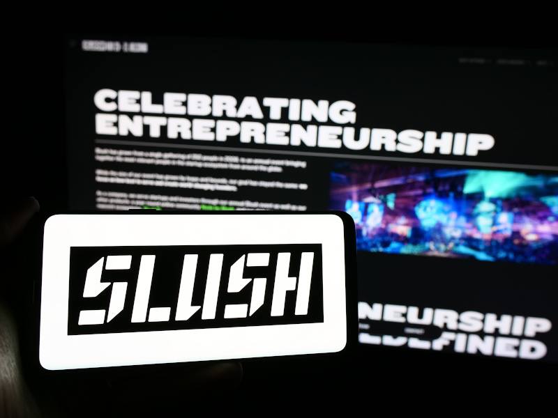 Person holding mobile phone with logo of Finnish annual start-up and technology event Slush in front of a business web page.