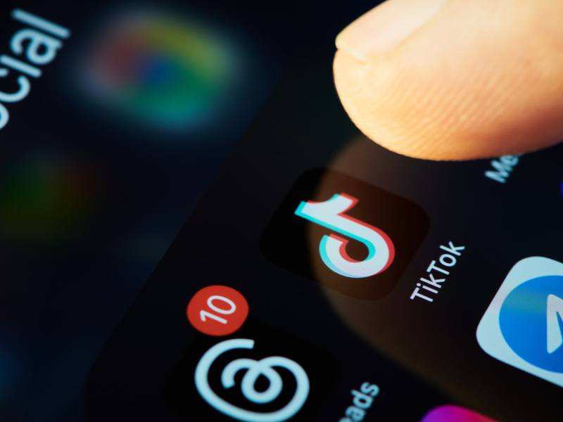 A close up of a person's finger touching the TikTok app on a smartphone.