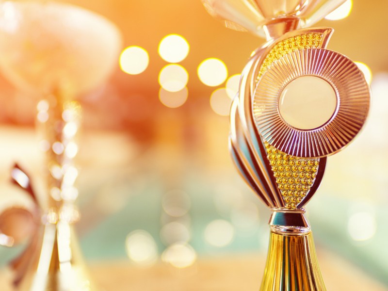 A gleaming golden trophy is on display. In the background, a separate golden trophy can be seen but is out of focus.