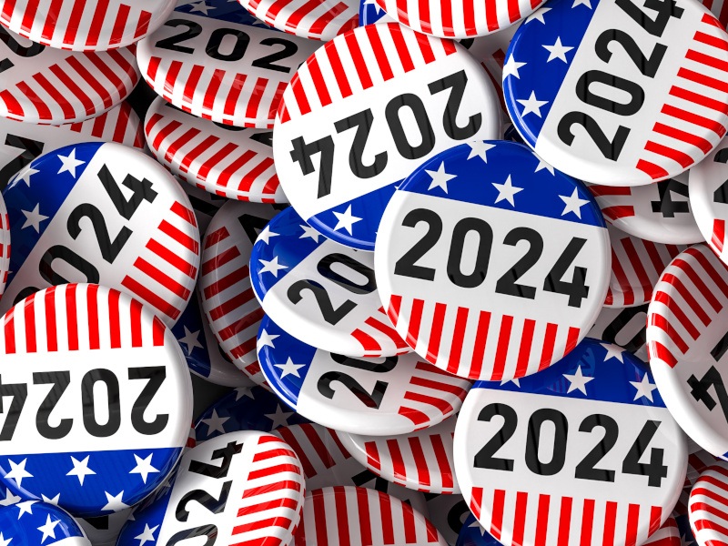 A number of US Presidential Election 2024 buttons are seen piled together, displaying the colours of the American flag: red, white and blue.