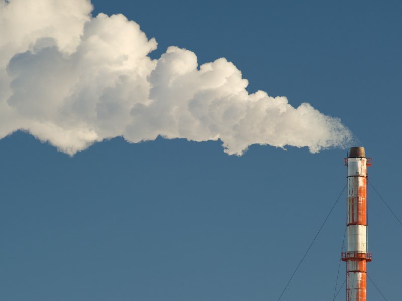 Smoke billows from a smokestack against a blue sky.