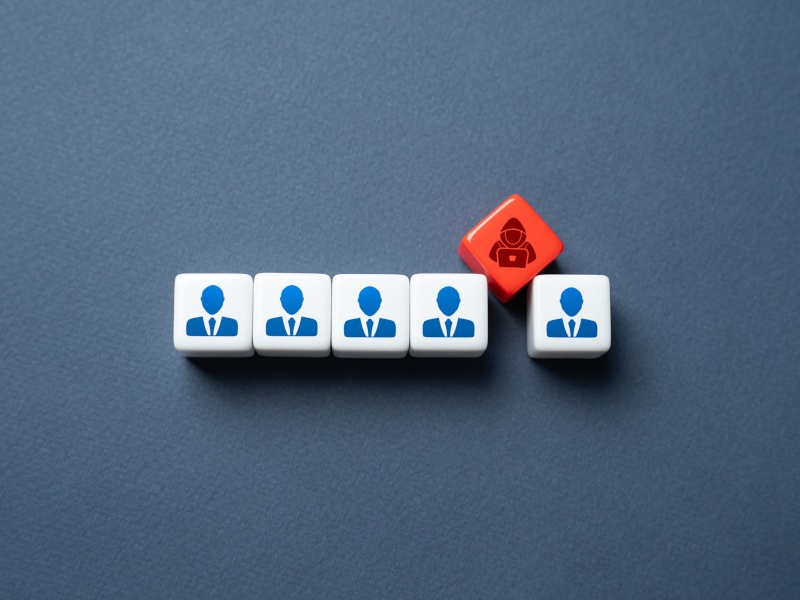 A row of five blocks depicting business people sit in a row, while a red block depicting a hacker slots itself between two of the blocks.