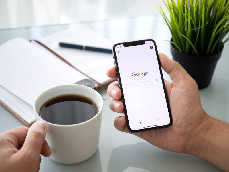 Man holding iPhone X with Google search page open.