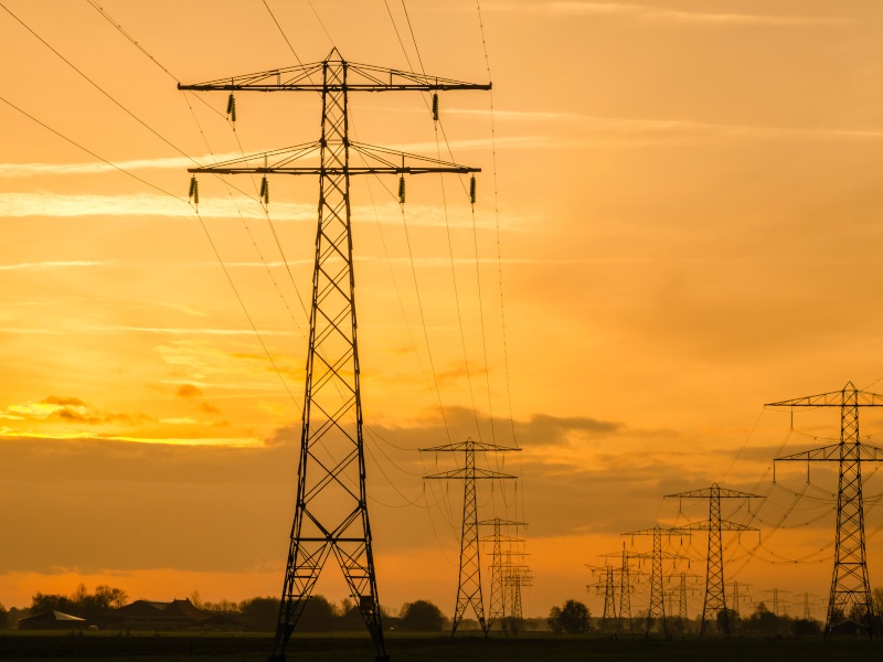 Power lines and transmission towers in a line across fields against a golden-orange sky.