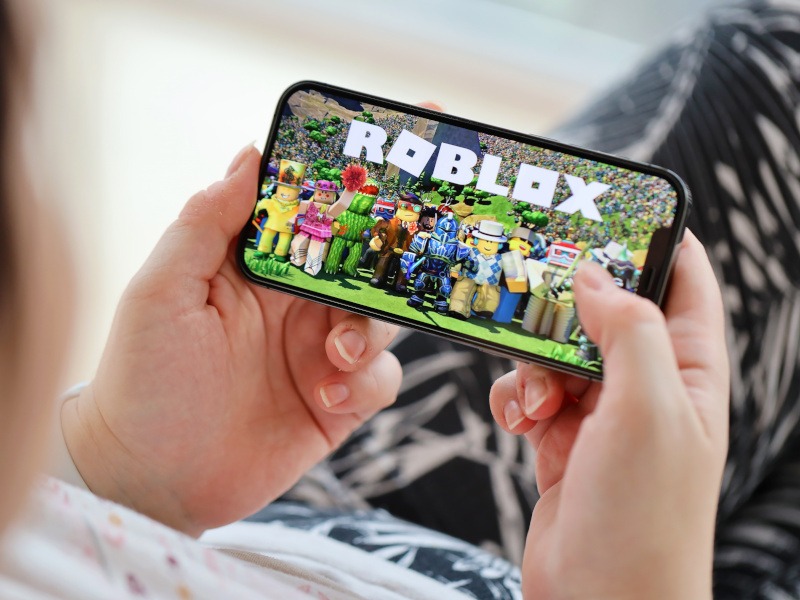 A child holding a smartphone and playing Roblox.