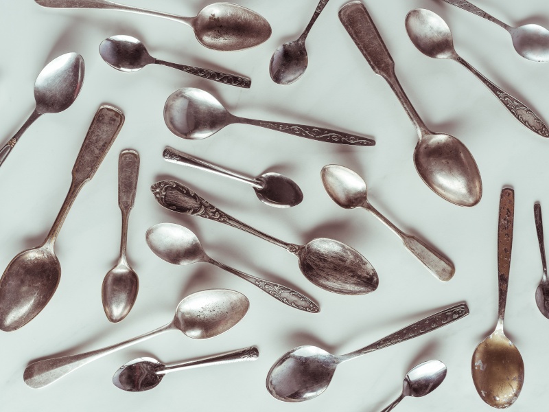 A bunch of vintage metal spoons scattered around a white surface.