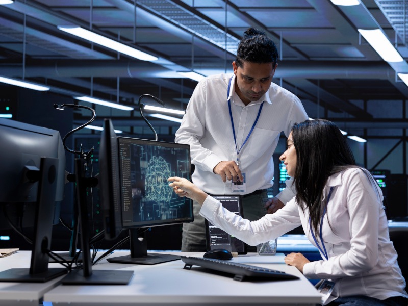 Two office workers examine a computer monitor showing data. They could be working for an AI tech company, such as Nebius.