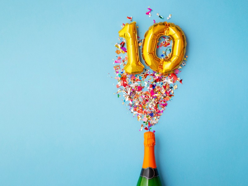 Blue background with a champagne bottle popping out the number 10 with confetti.