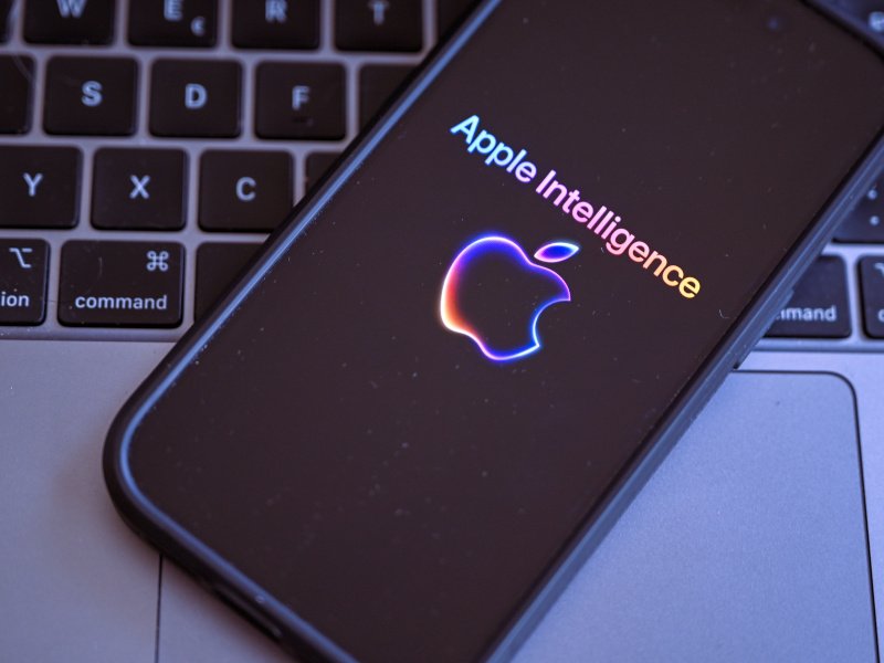 A smartphone displaying the ‘Apple Intelligence’ logo. The phone is placed on top of a keyboard.