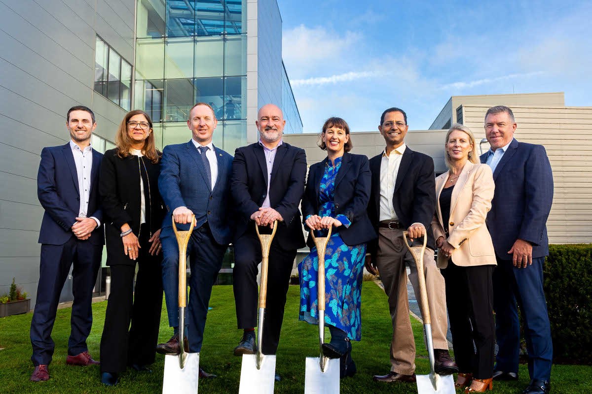 Eight people standing in a row with four in the centre holding shovels.