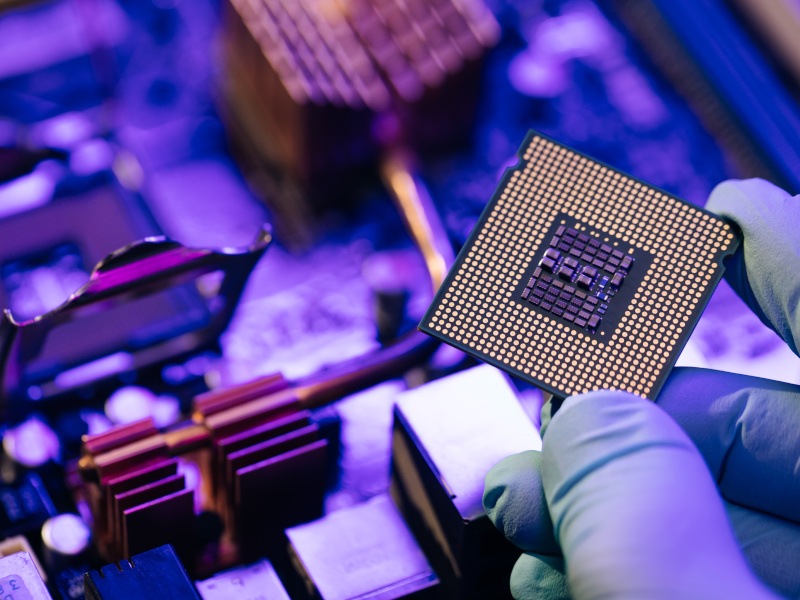 A computer chip being held up next to a circuit board. This photograph is meant to represent the chip maker Synopsis.