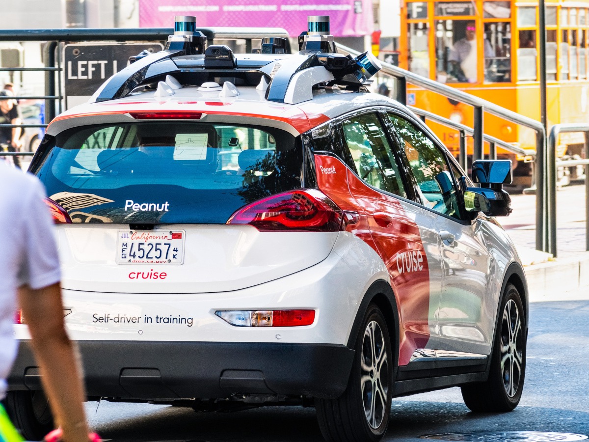 The back of a GM Cruise self-driving robotaxi on a city street on a sunny day.