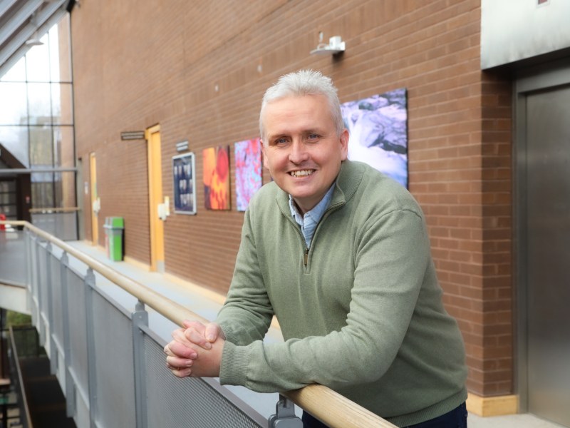 A man wearing a green jumper smiles as he leans over a railing at University of Limerick.