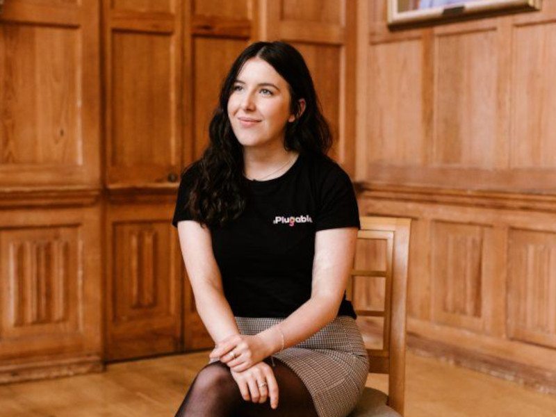 CEO and co-founder of start-up GoPlugable, Maebh Reynolds sitting in a chair in a room with wood panelling.