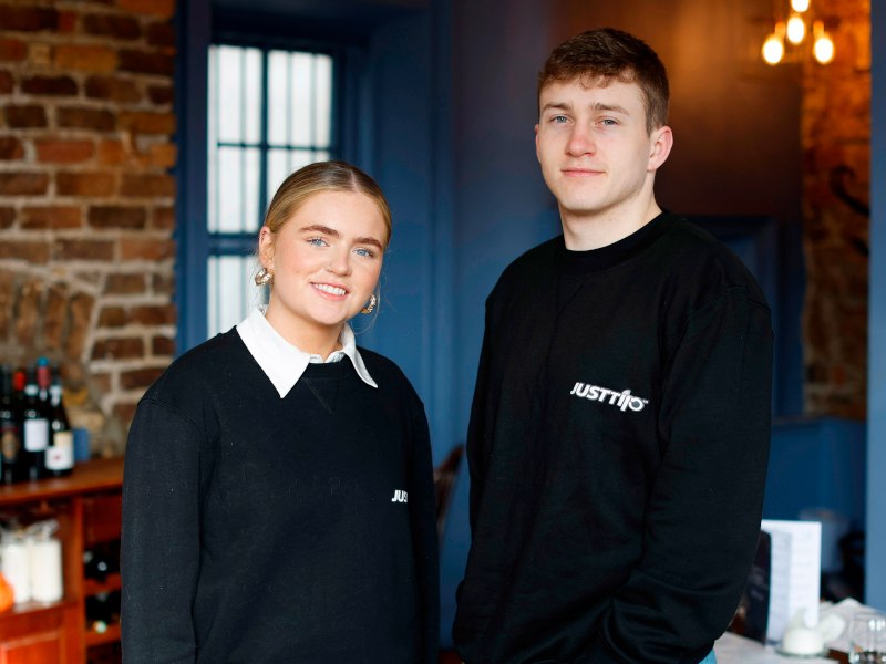 A woman and a man stand next to each other while smiling. They are both wearing dark jumpers with the 'JustTip' company name written on them.